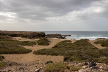 Açık kahverengi toprak, Atlantik Okyanusu kıyısındaki adanın batı kıyısında taş ve kayalarla dolu. Kışın yoğun bulutlar. Batı kıyısı (Playa de Jarubio bölgesi), Fuerteventura.