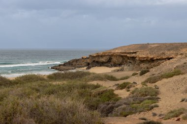 Açık kahverengi toprak, Atlantik Okyanusu kıyısındaki adanın batı kıyısında taş ve kayalarla dolu. Kışın yoğun bulutlar. Batı kıyısı (Playa de Jarubio bölgesi), Fuerteventura.