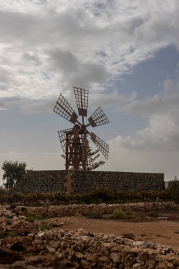 Taş tabanlı, iyi korunmuş eski bir yel değirmeni. Akşamın erken saatlerinde. Kışın yoğun bulutlu mavi gökyüzü. Tindaya, Fuerteventura, Kanarya Adaları.