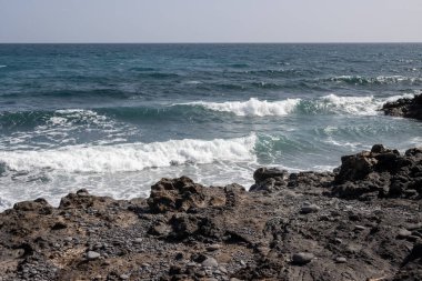 Küçük dalgalı Atlantik Okyanusu. Kıyıdaki siyah kayalar. Ufuktaki mavi gökyüzü. Fabrica de callao de los Pozos, Puerto del Rosario, Fuerteventura, İspanya.