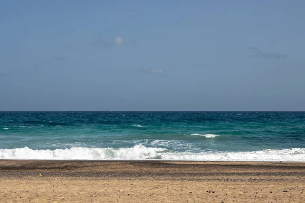 Atlantic ocean with small waves. Golden color of the sand. Blue sky on a horizon. Playa Blanca, Fuerteventura, Spain.