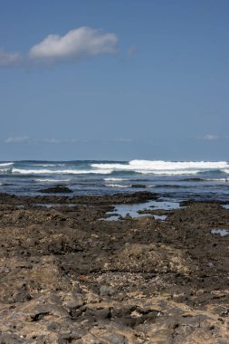 Adanın kuzeyindeki Rocky plajı. Kışın Atlantik okyanusu dalgaları. Çok açık bulutlu mavi bir gökyüzü. Playa del Bajo de la Burra ve Playa el Mejilon, Fuerteventura.