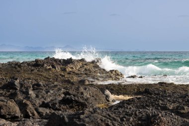 Avrupa 'nın eşsiz çölünün Atlantik okyanusuyla buluştuğu kıyı şeridinin kayalık kıyısı. Küçük dalgalar, mavi gökyüzü. Park Doğal Dunas de Corralejo, Fuerteventura, Kanarya Adaları.