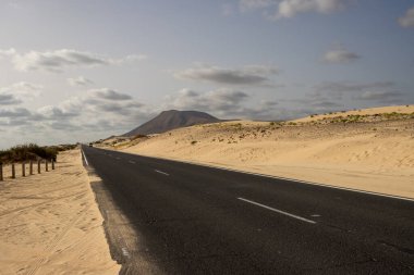 Çölde yol kalitesi iyi. Yolun iki tarafındaki kum tepelerinin kumları. Kış mevsiminde insan olmaz. Park Doğal Dunas de Corralejo, Fuerteventura, Kanarya Adaları, İspanya.
