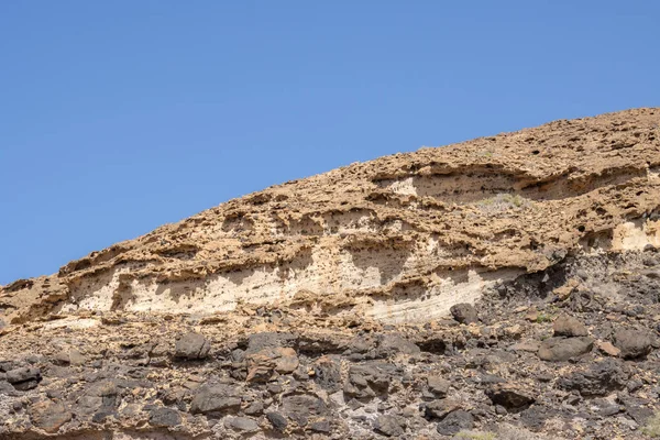 Detail of high rocky mountains with a dry surface in the winter.  Bright blue sky. Parque natural Jandia, Fuerteventura, Canary Islands, Spain.