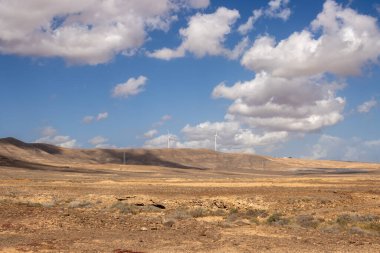 Başkent Puerto del Rosario 'dan adanın merkezine giderken yolda volkanik kayalık dağlar var. Rüzgar türbinleri. Beyaz bulutlu mavi gökyüzü. Fuerteventura, Kanarya Adaları.