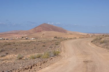 Adanın merkezindeki bir yaylanın etrafındaki kuru volkanik kayalık dağlar. Taşra yolu. Beyaz bulutlu mavi gökyüzü. Merkez Fuerteventura, Kanarya Adaları, İspanya.