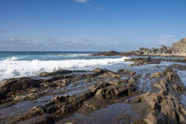 Adanın batısındaki Atlantik Okyanusu plajı. Koyu kahverengiden siyah kayalara doğal havuzlar oluşturur. Kışın güneşli bir gün. Aguas Verdes, Fuerteventura, Kanarya Adaları, İspanya.