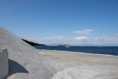 Adanın kıyısında mermer madenciliği. Parlak beyaz mermer bloklar halinde ya da taş gibi parçalar halinde. Mavi gökyüzü. Porto Vathy, Thassos (Thasos), Yunanistan.