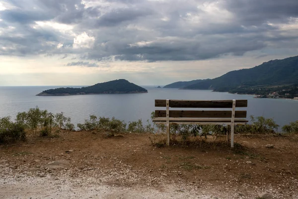 Early morning at a hill on the south of the island. Wooden empty bench with a view on the Thracian sea, little island and peninsula. Cloudy sky. Thassos (Thasos), Greece.
