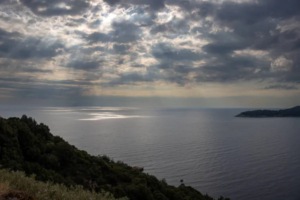 Diagonal line of a nature on a hill and view on the Thracian sea, enlightened by rays of sunshine cross an intense clouds in the late summer. South of Thassos (Thasos), Greece.