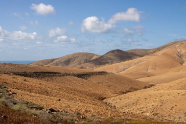 Adanın merkezindeki tepeler ve dağlar. Bir sürü taş ve kayadan oluşan kuru kumlu toprak. Beyaz bulutlu mavi gökyüzü. Fuerteventura, Kanarya Adaları, İspanya.
