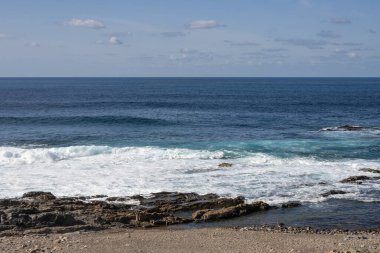 Atlantik Okyanusu kıyısında kayalık bir sahil. Kışın sakin su. Mavi gökyüzü ve ışık bulutları. Aquas Verdes, Playa del Valle, Fuerteventura, Kanarya Adaları, İspanya.