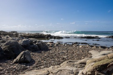 Atlantik Okyanusu kıyısında kayalık bir sahil. Kışın sakin su. Mavi gökyüzü ve ışık bulutları. Aquas Verdes, Playa del Valle, Fuerteventura, Kanarya Adaları, İspanya.
