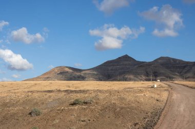 Adanın merkezindeki dağlar, Tindaya kasabasına yakın. Dağlara giden taşra yolu. Beyaz bulutlu mavi gökyüzü. Fuerteventura, Kanarya Adaları, İspanya.