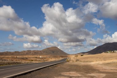 Adanın merkezindeki Tindaya kasabasına yakın dağlara giden bir vadide yol. Kış mevsiminde trafik olmaz. Beyaz bulutlu mavi gökyüzü. Fuerteventura, İspanya.