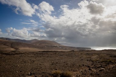 Kuru volkanik kara ve Atlantik Okyanusu, adanın batısında. Yoğun beyaz bulutlar. Yürüyüş için yer var. Gambuesa de Llano del Sombrero, Betancuria, Fuerteventura, Kanarya Adaları.