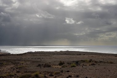 Kuru volkanik kara ve Atlantik Okyanusu, adanın batısında. Yoğun beyaz bulutlar. Yürüyüş için yer var. Gambuesa de Llano del Sombrero, Betancuria, Fuerteventura, Kanarya Adaları.