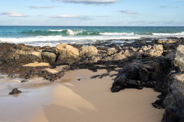 Atlantik Okyanusu sahilinde kum ve kayalık bir sahil kombinasyonu. Beyaz bulutlu mavi gökyüzü. Park Natural Dunas de Corralejo, Fuerteventura, İspanya.