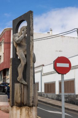 Çerçevenin arkasında küçük bir kertenkele oturan bir adamın ahşap heykeli. Giriş trafik işareti yok. Beyaz bulutlu mavi gökyüzü. Puerto del Rosario, Fuerteventura, İspanya.