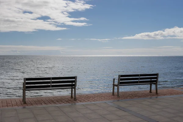 stock image Promenade at the coast of the Atlantic ocean. Two empty benches to enjoy the view. Blue sky with white clouds. Tarajalejo, Fuerteventura, Canary Islands, Spain.