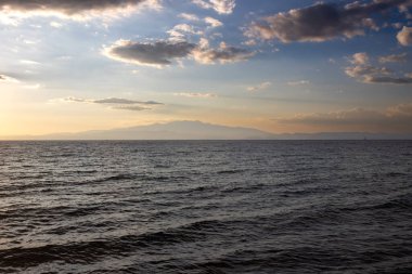 Altın saat boyunca Ege Denizi 'nin (Akdeniz) sakin suları. Yunanistan kıtasının dağları ufukta belirdi. Yazın sonlarında gökyüzü açık bulutlu. Thassos (Tassos) batı, Yunanistan.