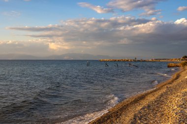 Adanın batısındaki bir sahilde altın saat. Arka planda Yunanistan kıta dağları var. Mavi gökyüzü ve ışık bulutları. Thassos (Tassos), Yunanistan.