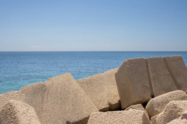Betondan yapılmış devasa kübik nesneler, yerel marinada deniz kenarı olarak kullanılıyor. Akdeniz 'in sakin suları (Tyrhenian). Baharın başlarında mavi gökyüzü. Marsala, Batı Sicilya, İtalya.