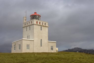 Deniz fenerinin sahil manzarası. Sonbaharda yoğun yağmur bulutları. Arka plandaki dağ. Yeşil çimenler. Dyrholaey, İzlanda.