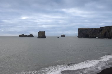 Adanın güneyindeki Atlantik Okyanusu kıyısı. Kaya oluşumlarıyla ünlü kara kumlu bir sahil. Sonbaharda bulutlu bir gökyüzü. Reynisfjara, İzlanda.