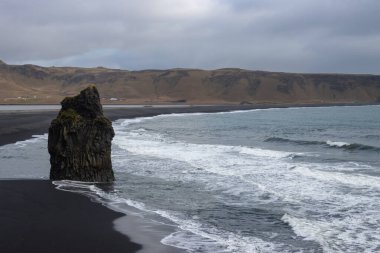 Adanın güneyindeki Atlantik Okyanusu kıyısı. Kaya oluşumlarıyla ünlü kara kumlu bir sahil. Sonbaharda bulutlu bir gökyüzü. Reynisfjara, İzlanda.