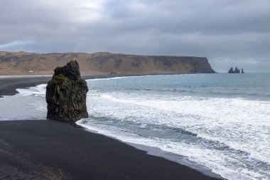 Adanın güneyindeki Atlantik Okyanusu kıyısı. Kaya oluşumlarıyla ünlü kara kumlu bir sahil. Sonbaharda bulutlu bir gökyüzü. Reynisfjara, İzlanda.