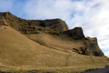 Dağların dramatik ve vahşi güzelliği ve otlar, yosunlar ve yosunlarla kaplı sakin otlaklar. Sonbaharda bulutlu bir gökyüzü. Vik, İzlanda.