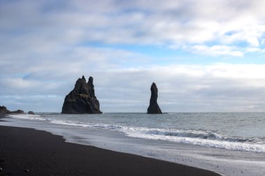 Adanın güneyindeki Atlantik Okyanusu kıyısı. Kaya oluşumlarıyla ünlü kara kumlu bir sahil. Sonbaharda bulutlu bir gökyüzü. Reynisfjara, İzlanda.