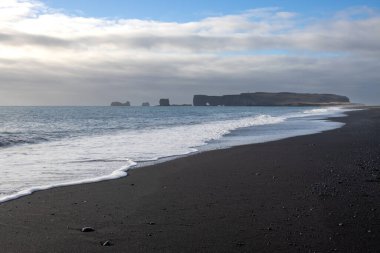 Adanın güneyindeki Atlantik Okyanusu kıyısı. Kaya oluşumlarıyla ünlü kara kumlu bir sahil. Sonbaharda bulutlu bir gökyüzü. Reynisfjara, İzlanda.