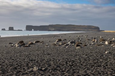 Adanın güneyindeki Atlantik Okyanusu kıyısı. Kaya oluşumlarıyla ünlü kara kumlu bir sahil. Sonbaharda bulutlu bir gökyüzü. Reynisfjara, İzlanda.