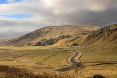 Dağların dramatik ve vahşi güzelliği ve otlar, yosunlar ve yosunlarla kaplı sakin otlaklar. Sonbaharda bulutlu bir gökyüzü. Vik, İzlanda.