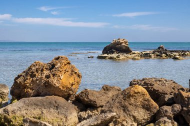 Kumsalın parlak ve berrak suyu. Sudaki küçük kayalar. Baharın başlarında mavi gökyüzü. Spiaggia Renella, Sicilya 'nın güneyi, İtalya.