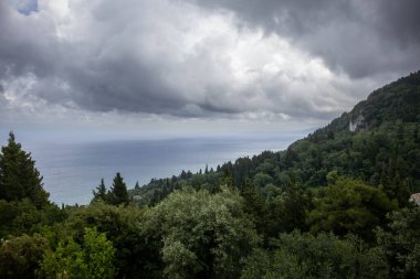 Uçurumun manzarası, çeşitli yeşillikler, ağaçlar ve çalılarla kaplı. İyon denizi ve yoğun bulutlu yağmurlu bir gökyüzü. Yer, İmparatoriçe Sisi için bir sağlık merkeziydi. Achilleio, Korfu, Yunanistan.