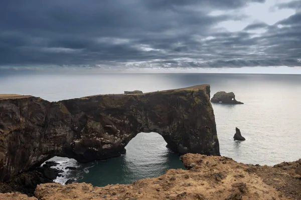 Famous Dyrholaey Arch, window in a rock in the Atlantic ocean. Cloudy sky in the autumn, reflecting some sunshine among the clouds. Dyrholaey, south Iceland.