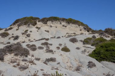 Adanın kıyısındaki tepe, sonbaharda çok kuru kumlu bir toprak ile. Çalıların çoğu da kurudu, bazıları yeniden tazelendi. Parlak mavi gökyüzü. Erikousa, Yunanistan.