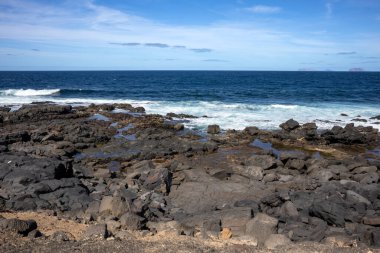 Atlantik Okyanusu kıyısında karanlık kayalar. Sakin mavi su. Mavi gökyüzü ve ışık bulutları. Lanzarote, Kanarya Adaları, İspanya.