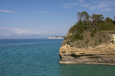 Adanın kuzey kesimindeki İyon (Akdeniz) kıyısında doğal kaya oluşumları. Denizin sakin suları. Baharda açık bulutlu mavi gökyüzü. Sidari, Korfu, Yunanistan.