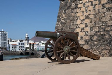 Aziz Gabriel Kalesi 'nin önündeki eski tarihi top. Kalenin duvarı. Köprü, kilise kulesi ve arka planda şehrin evleri. Parlak mavi gökyüzü. Arrecife, Lanzarote, Kanarya Adaları, İspanya.