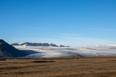 Avrupa 'nın en büyük buzulunun etrafındaki sonbahar ülkesi. Dağlar ve tarlalar buzulun güzelliğinin altını çiziyor. Vatnajokull, Güneydoğu İzlanda.
