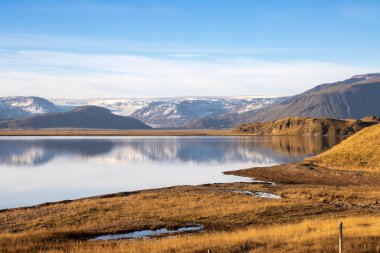 Sonbaharda tarlalarda sarı çimenler. Fiyort 'un çivit mavisi suyu, bu ada için tipik. Suyu çevreleyen dağlar. Mavi gökyüzü ve ışık bulutları. Doğu İzlanda.