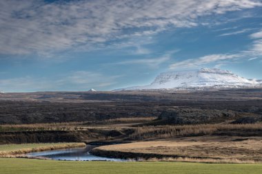 Nehirli bir kara parçası. Arkasında kar olan dağlar. açık beyaz bulutlu mavi gökyüzü. Borgarfjordur, Kuzey-Doğu İzlanda.