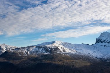 Dağlarla çevrili bir vadinin manzarası, hafif bir kar tabakasıyla. Yapılandırılmış beyaz bulutlu mavi gökyüzü. Borgarfjordur, Kuzey-Doğu İzlanda.