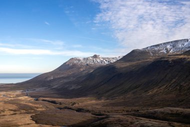 Adanın kuzeydoğusunda sonbahar doğası. Fiyort 'un etrafındaki görkemli dağlar, yosun ve yosunlarla kaplı. Atlantik okyanusunun sakin suları. Mavi gökyüzü ve ışık bulutları. Hafnarholmi, İzlanda.