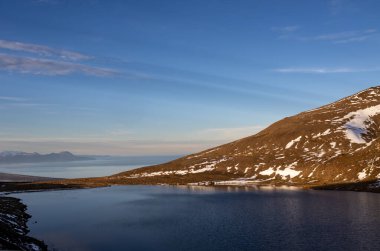 Adanın kuzeydoğusunda sonbahar doğası. Fiyort 'un etrafındaki görkemli dağlar, yosun ve yosunlarla kaplı. Atlantik okyanusunun sakin suları. Mavi gökyüzü ve ışık bulutları. Hafnarholmi, İzlanda.